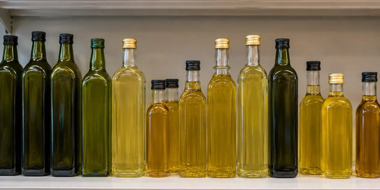 Row of unbranded olive oil bottles in varied shapes along a clean pale grocery shelf in daylight