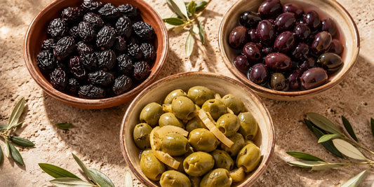 Overhead view of Moroccan olives in terracotta dishes: dry black, glossy purple, and cracked green with preserved lemon
