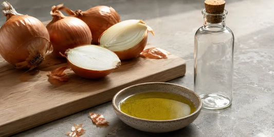 Whole and halved brown onions on an oak board beside a dish of golden-green olive oil