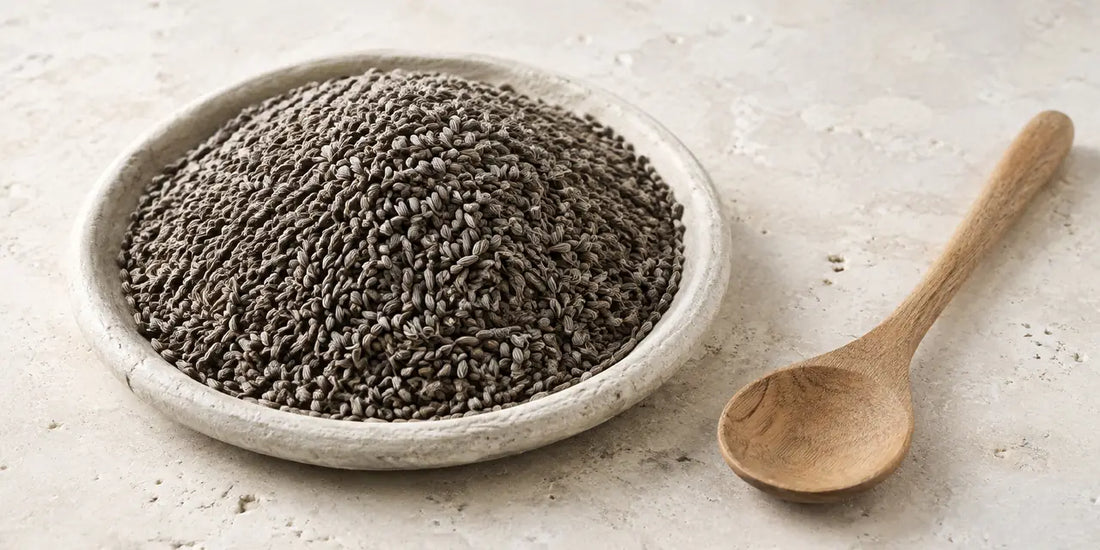 Small greyish-brown kidney-shaped seeds heaped in a shallow stone dish beside a plain wooden spoon