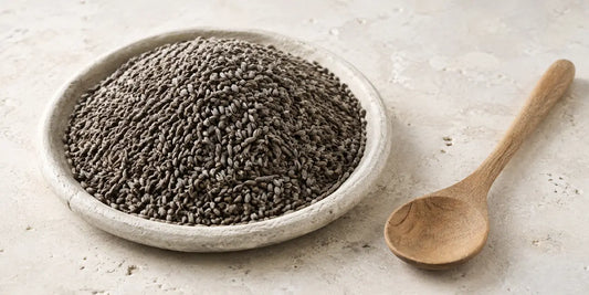 Small greyish-brown kidney-shaped seeds heaped in a shallow stone dish beside a plain wooden spoon