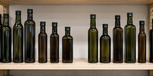 Row of unbranded dark green and amber glass oil bottles of varied heights on pale grocery shelf