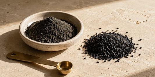 Pale ceramic dish of milled dark seed powder beside heap of whole matte black seeds on stone