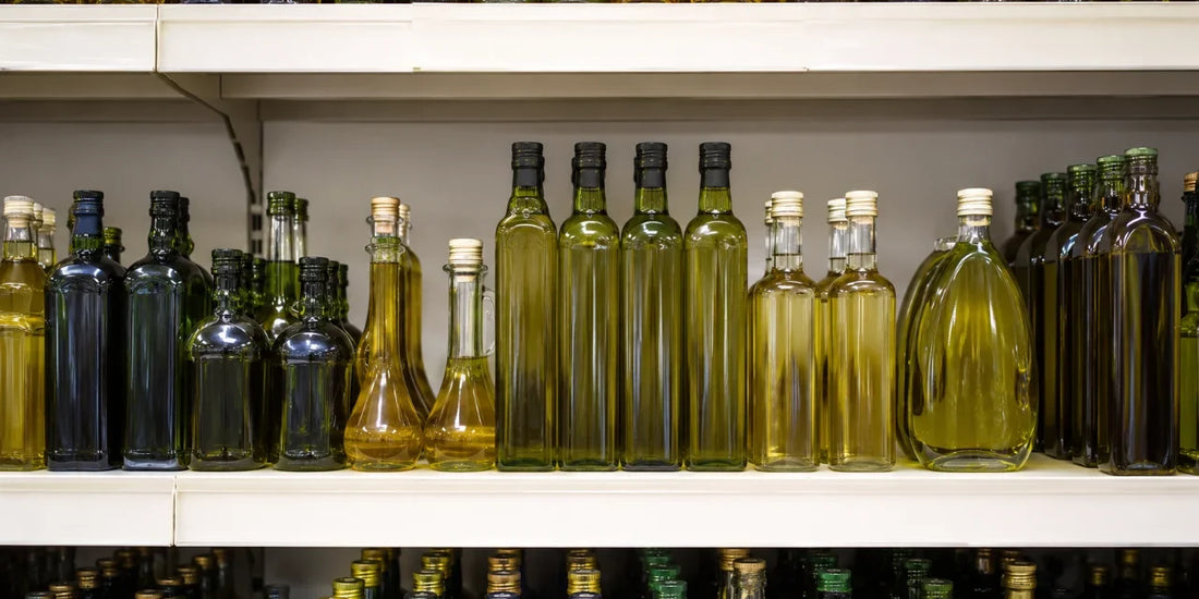 A tidy grocery shelf of unlabelled tall and short olive oil bottles in soft even light