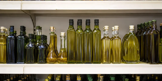 A tidy grocery shelf of unlabelled tall and short olive oil bottles in soft even light