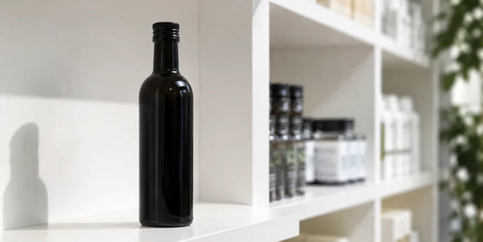 A single dark glass black seed oil bottle on a clean white pharmacy-style shelf in soft directional light