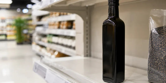 A single dark glass black seed oil bottle on a clean supermarket-style shelf in soft directional light