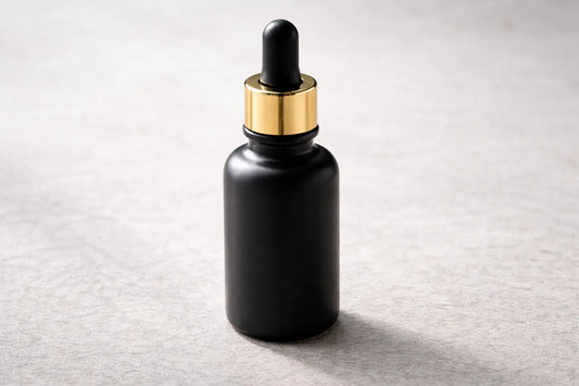 Matte black glass bottle of black seed oil with gold dropper on a neutral stone surface in calm lighting