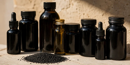 Row of varied unbranded dark glass bottles behind a small heap of matte black seeds on pale stone