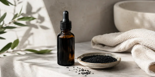 Dark glass dropper bottle of deep amber black seed oil with a small dish on a pale stone shelf in soft daylight