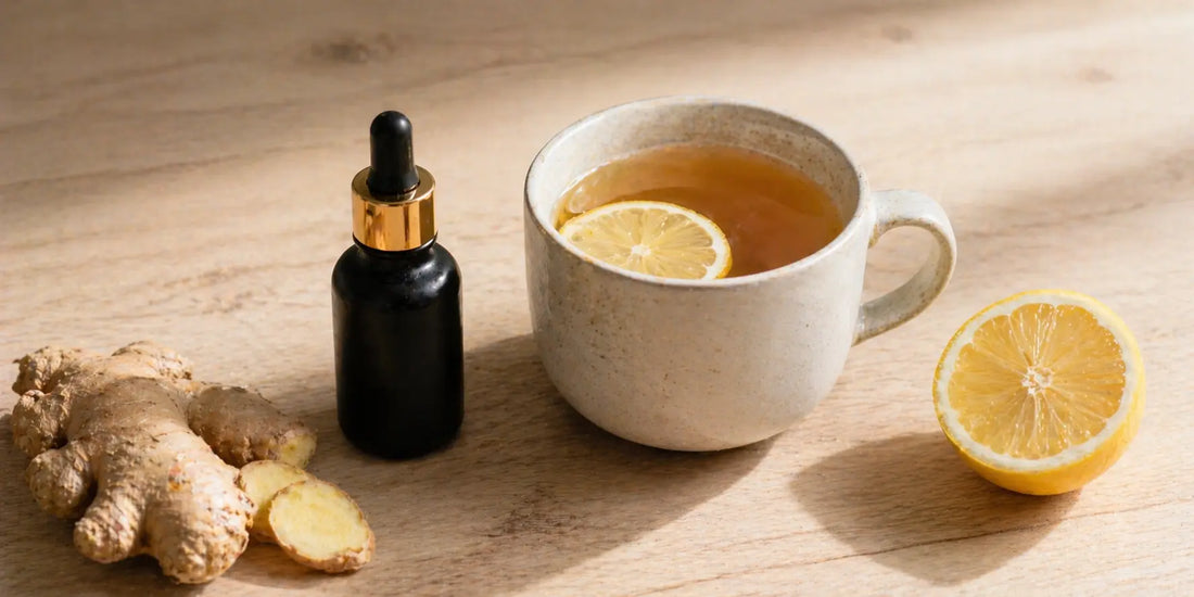 Matte black glass bottle of black seed oil beside a ceramic mug of amber lemon-ginger tea with fresh ginger root