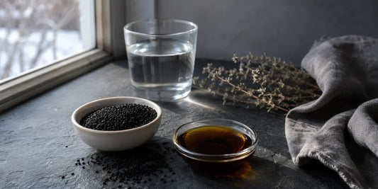 Black cumin seeds, a dish of deep bronze black seed oil and a glass of water on a winter windowsill