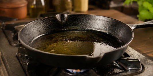 A cast iron skillet with a shimmering pool of golden cooking oil over a low flame