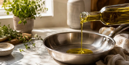 Rich golden-green olive oil pouring from a glass bottle into a pan on a bright kitchen worktop