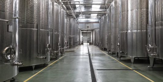 Rows of tall stainless steel olive oil storage tanks inside a large industrial processing facility