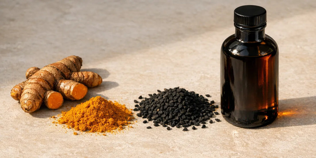 Whole turmeric root, golden-orange turmeric powder, matte black cumin seeds and a dark glass oil bottle on pale stone