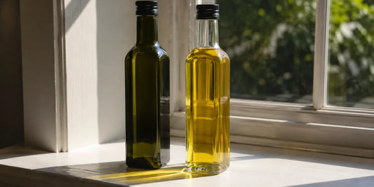 Dark green and clear olive oil bottles side by side on a sunlit windowsill in hard directional light