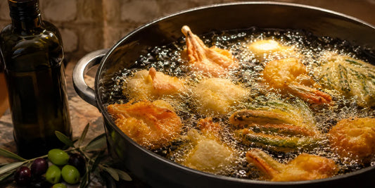 Golden food frying in a deep pan of hot olive oil with a dark glass bottle and olives nearby