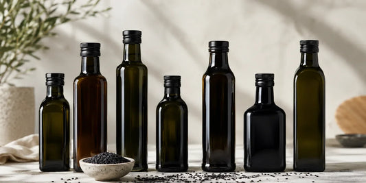 Several unbranded dark glass oil bottles of varied shapes on a clean light surface in soft directional daylight, conveying choice