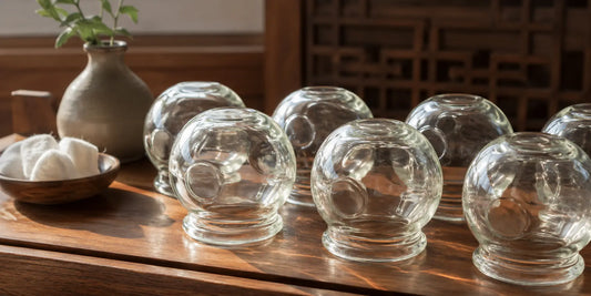 A set of traditional rounded glass cupping vessels arranged on a clean wooden surface in soft directional light
