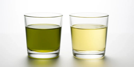 Two identical glasses backlit on white, the left holding vivid emerald green-gold oil and the right pale straw oil