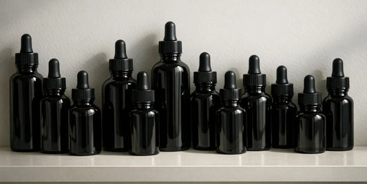 Row of unbranded dark glass dropper bottles of varied heights on a clean pale shelf in soft light