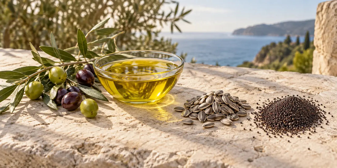Bowl of rich golden-green olive oil beside an olive branch, sunflower seeds and rapeseed on pale stone
