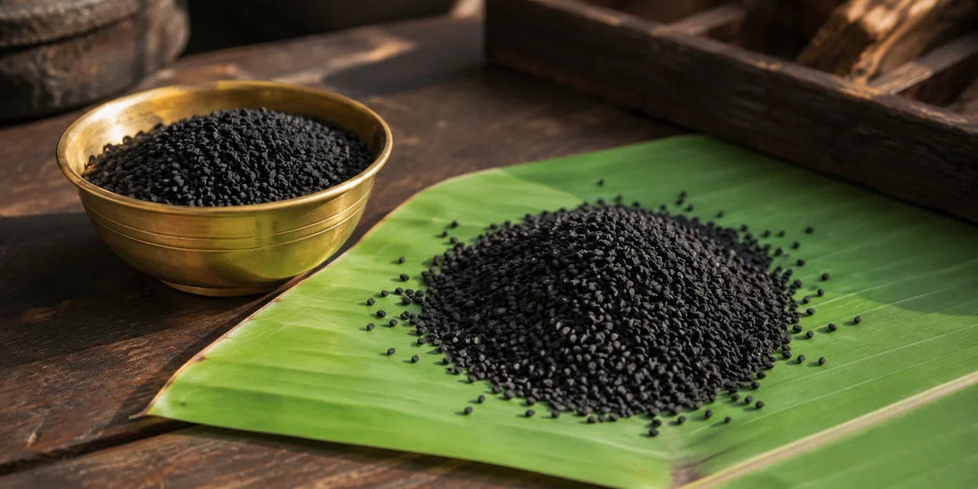 Heap of matte black angular nigella seeds on a fresh green banana leaf beside a small brass bowl