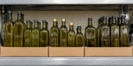Rows of plain unbranded dark glass olive oil bottles in open cardboard trays on a steel supermarket shelf