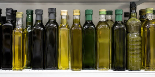 A row of varied unbranded olive oil bottles on a bright supermarket shelf, some clear and pale, in soft even daylight