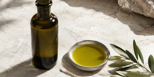 Dark glass extra virgin olive oil bottle of rich golden-green oil beside a cotton bud and olive leaves on pale stone