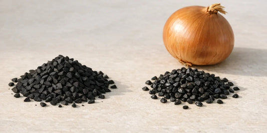 Two small heaps of dark seeds side by side on pale stone with a whole brown-skinned onion behind them