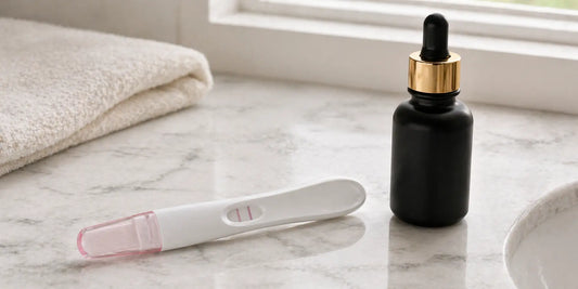 A positive pregnancy test and a matte black glass bottle of black seed oil on a pale bathroom counter