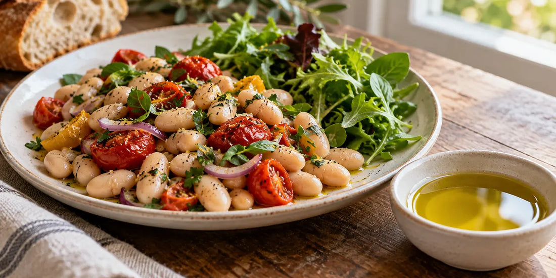 White bean and tomato salad beside a ceramic bowl of golden-green olive oil on a sunlit wooden table