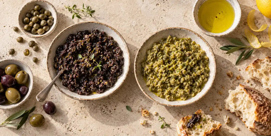 Two ceramic bowls of black and green tapenade with olives, capers, bread and golden-green oil