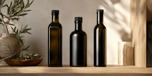 Three different dark glass bottles of oil arranged in a row on a pale wooden shelf in soft natural daylight