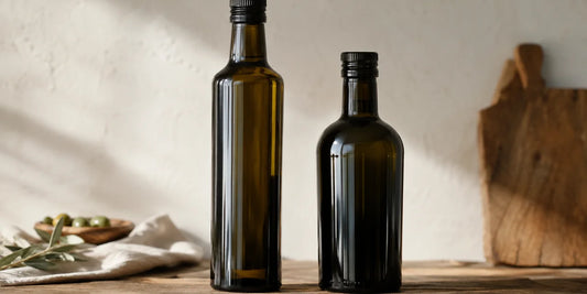 Two unbranded dark glass oil bottles of different shapes standing side by side on a worn wooden surface